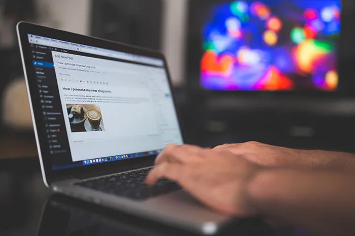 A blogger typing a post titled 'How I promote my new blog post' in the WordPress editor on a laptop